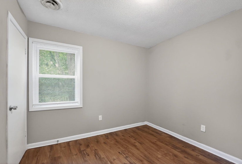 Neutral painted walls with white trim, wood-finish flooring, and a single window with blinds