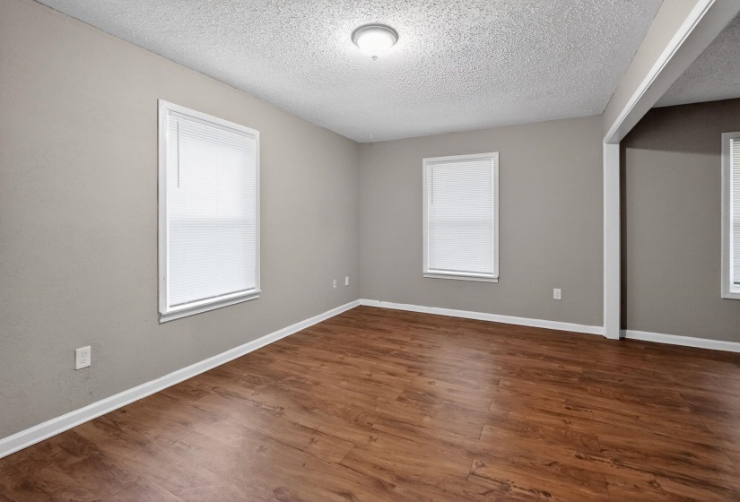 Spacious room featuring wood-finish flooring, neutral gray walls, and multiple windows with blinds