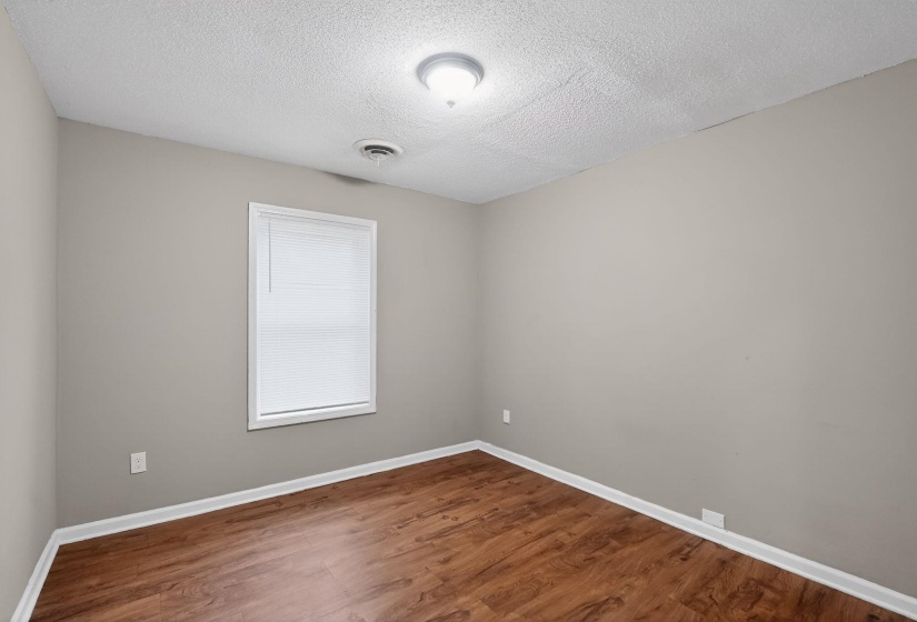 Neutral-toned room featuring wood-finish flooring, white baseboards, and a window with blinds