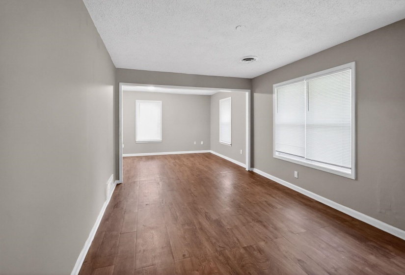 Expansive room featuring wood-finish flooring, neutral gray walls, white trim, and multiple windows with blinds