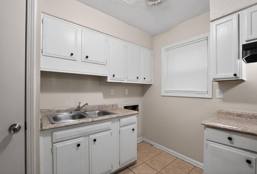Kitchen featuring white cabinetry, a double basin stainless steel sink, a window with horizontal blinds, and tile flooring
