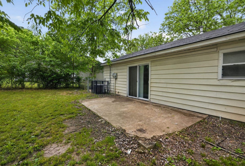 Expansive backyard featuring a concrete patio, sliding glass door access to the interior, horizontal siding, and a partial fence line with mature trees