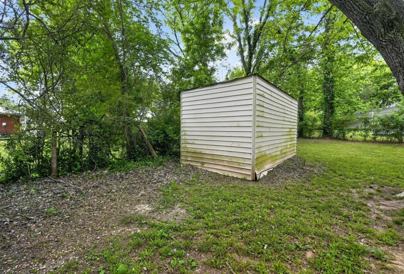 Detached storage shed with horizontal siding, surrounded by mature trees and a grassy yard