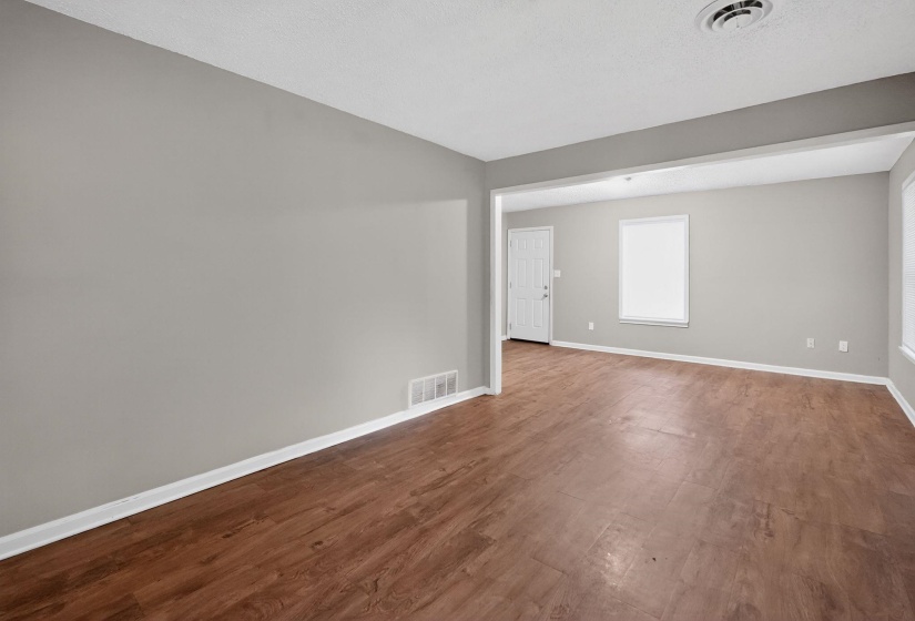 Expansive living area featuring wood-finish flooring, light gray walls, white baseboards, and multiple windows
