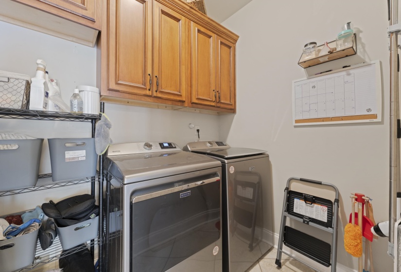 Laundry area featuring light wood-finish cabinetry, a white wall-mounted calendar, and a wall-mounted wire shelf
