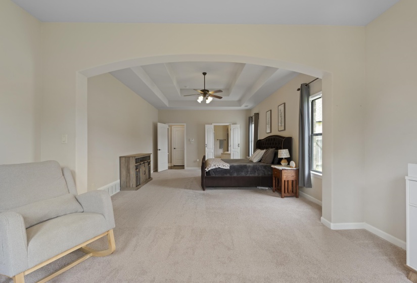 Spacious bedroom featuring an arched entryway, tray ceiling, ceiling fan, and carpeted flooring