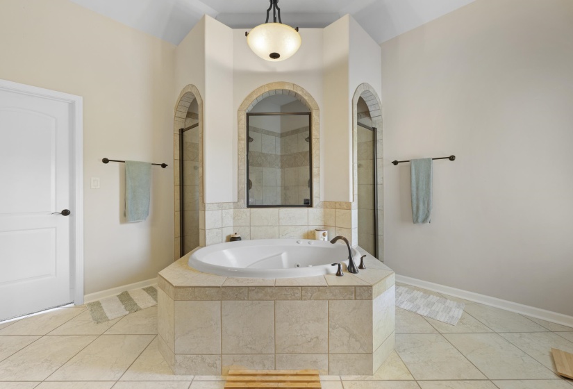 Soaking tub with tiled surround, flanked by two arched shower enclosures