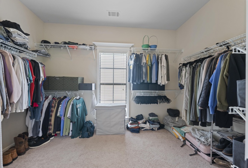 Spacious walk-in closet featuring light-colored carpeting, a window with blinds, and extensive wire shelving and hanging rods