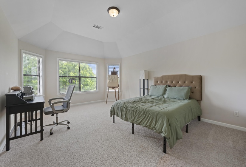 Bright bedroom featuring multiple windows with blinds, vaulted ceilings, and light-toned carpet flooring