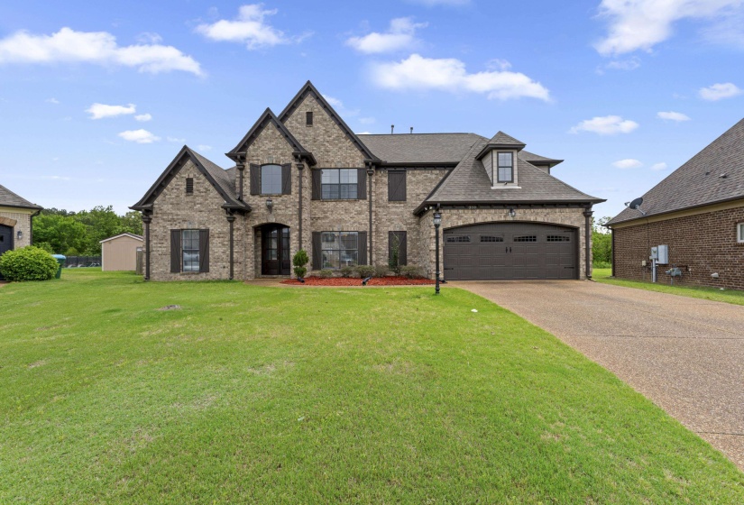 Traditional brick residence featuring a two-car garage with an arched door, a dormer window, and an arched entry door