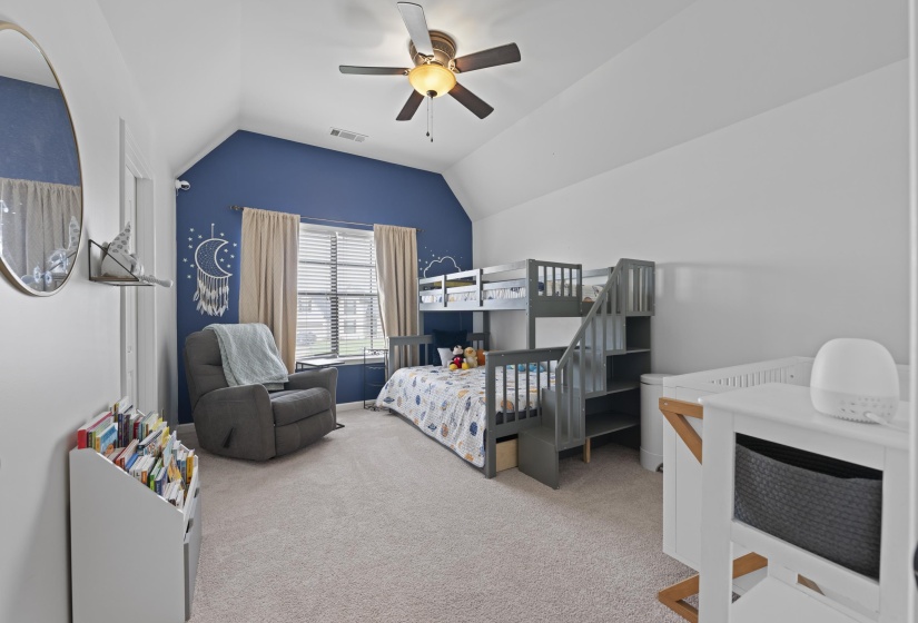 Carpeted bedroom featuring an accent wall, vaulted ceiling, ceiling fan with light, and a window with blinds