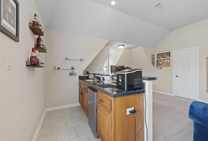 Wet bar featuring wood cabinetry, dark stone countertop, undermount sink, and stainless steel compact refrigerator