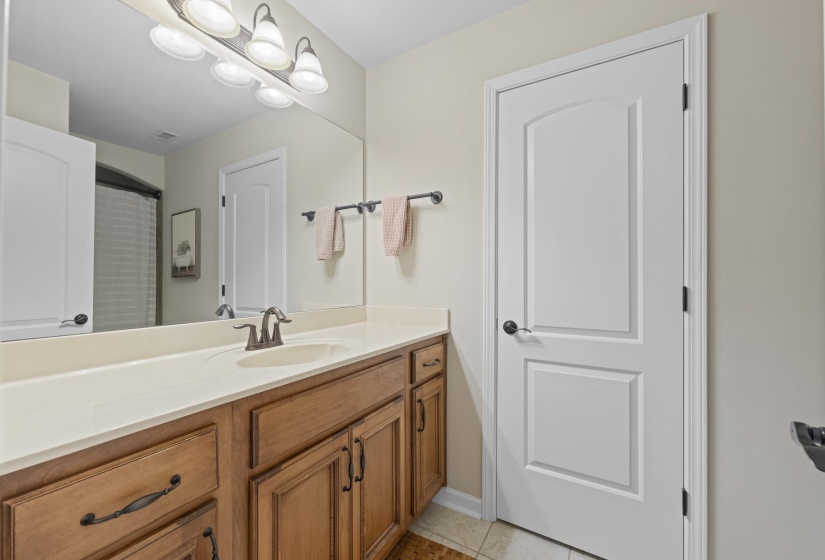 Bathroom vanity featuring wood-finish cabinetry with dark hardware, a light-toned countertop, and an integrated sink with a brushed metal faucet