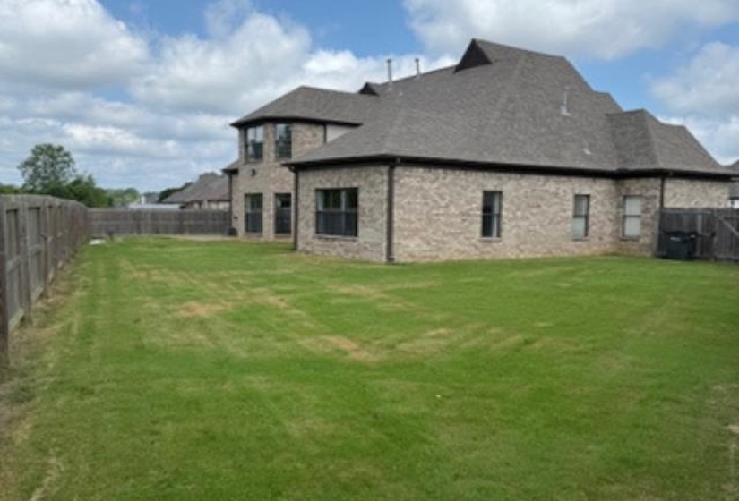 Expansive backyard featuring a manicured lawn, full privacy fencing, and a two-story brick exterior with multiple windows