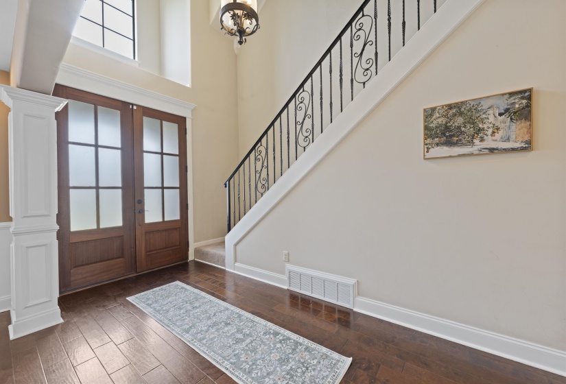 Grand entry featuring double wood doors with frosted glass panels, wood-finish flooring, a two-story ceiling, and a staircase with wrought iron balusters