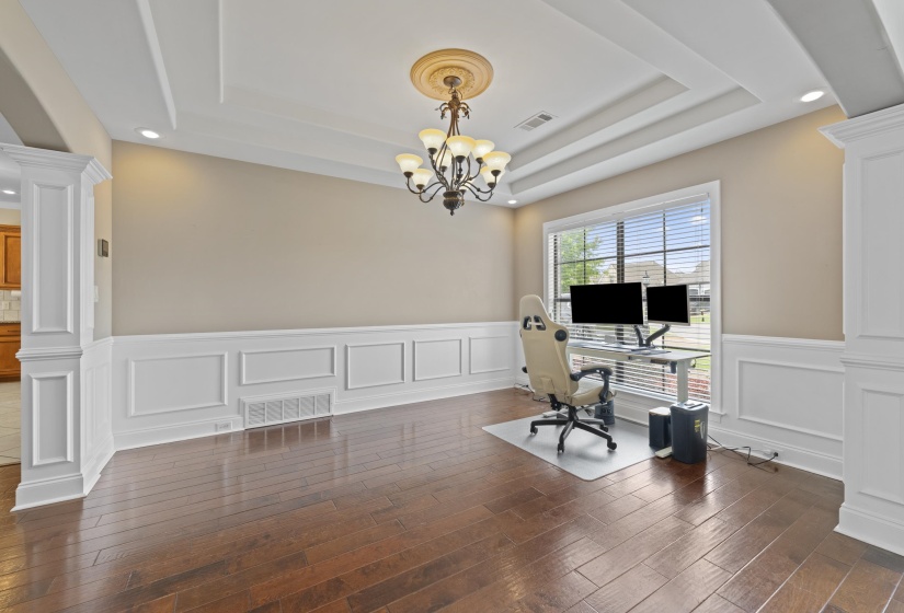 Spacious room featuring rich wood-finish flooring, elegant wainscoting, and a detailed coffered ceiling with recessed lighting