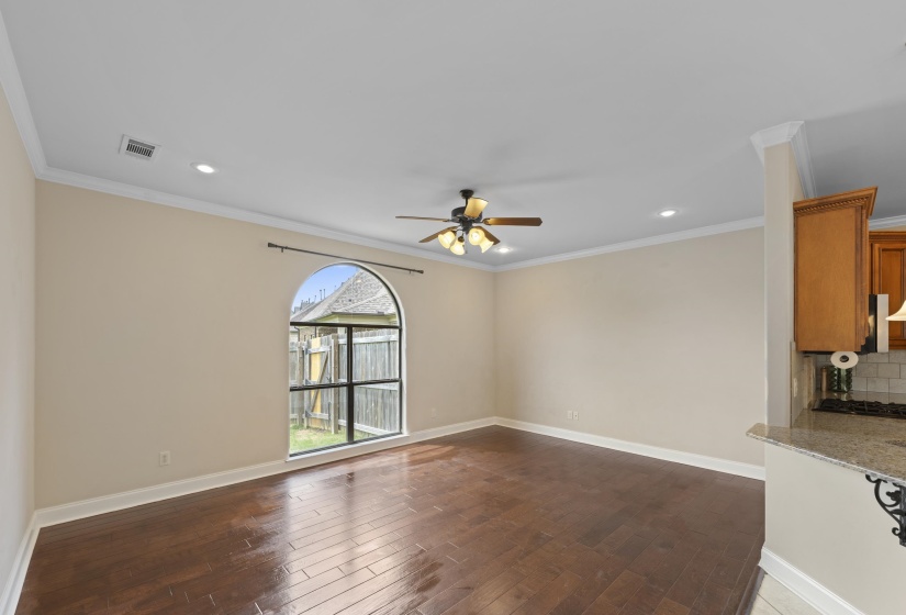 Spacious room featuring wood-finish flooring, a large arched window with a black frame, and a ceiling fan with integrated lighting