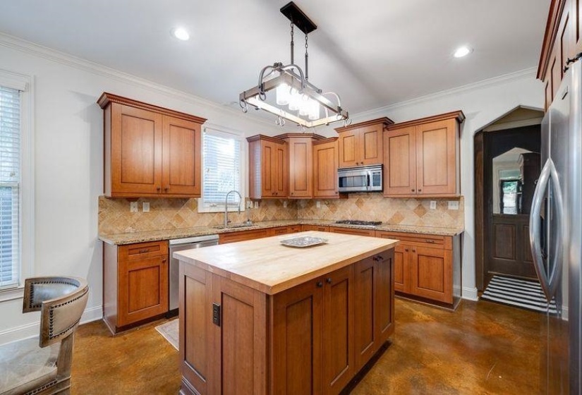 Kitchen with sink, wooden counters, decorative light fixtures, appliances with stainless steel finishes, and a center island