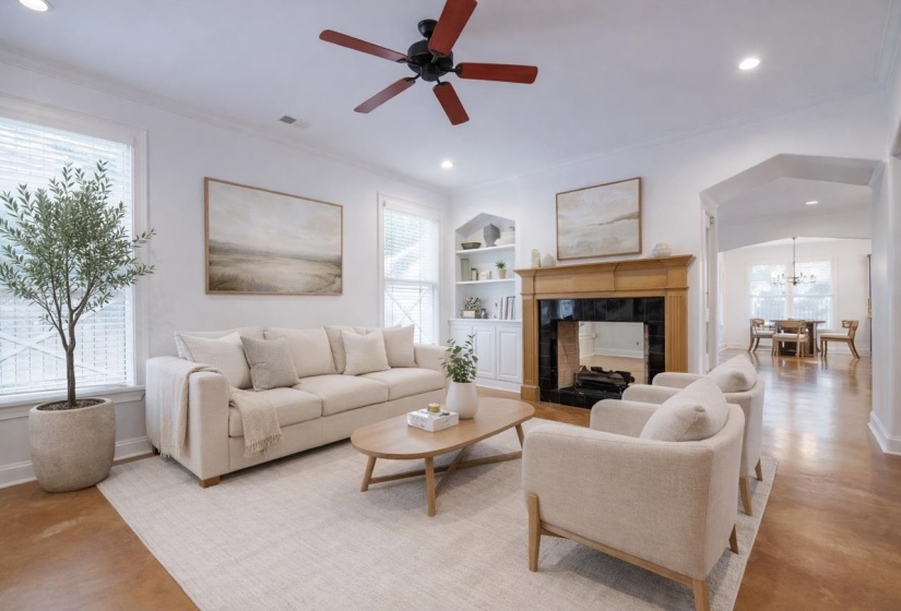 Living room featuring built in shelves, concrete flooring, a ceiling fan, a tiled fireplace, and crown molding