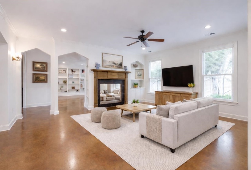 Living area with ceiling fan, built in shelves, a multi sided fireplace, concrete flooring, and crown molding