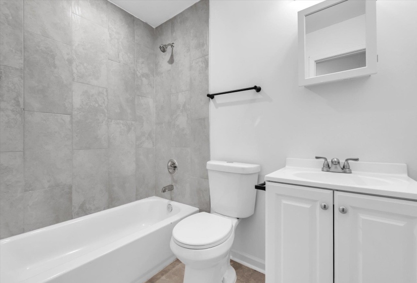 Bathroom featuring a white bathtub with chrome fixtures, light gray subway tile surround, white toilet, and a white vanity with an integrated sink and medicine cabinet