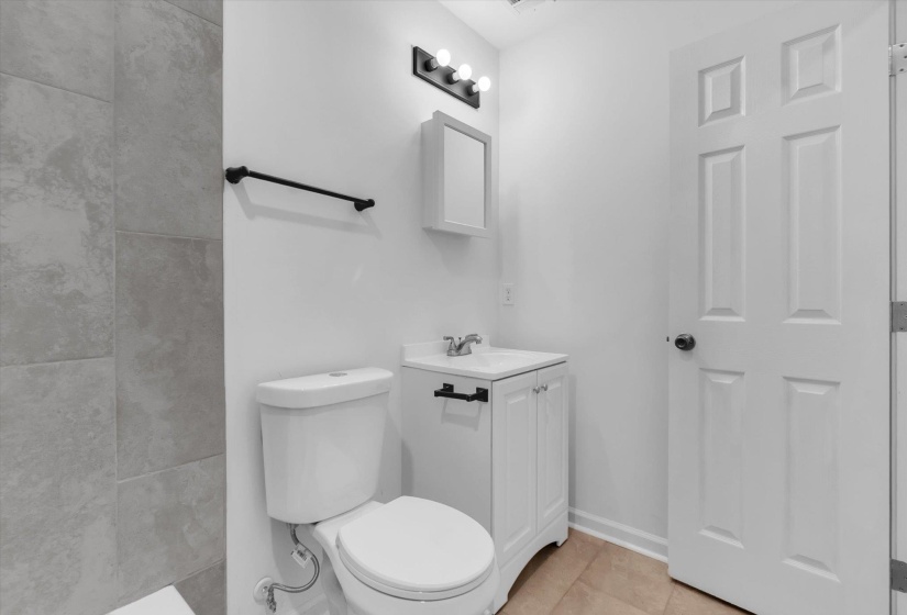 Bathroom featuring light gray wall tile, a white vanity with panel doors, a white medicine cabinet, a three-bulb sconce, and tan floor tiling