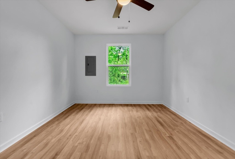 Spacious interior room with wood-finish flooring, white baseboards, and a ceiling fan