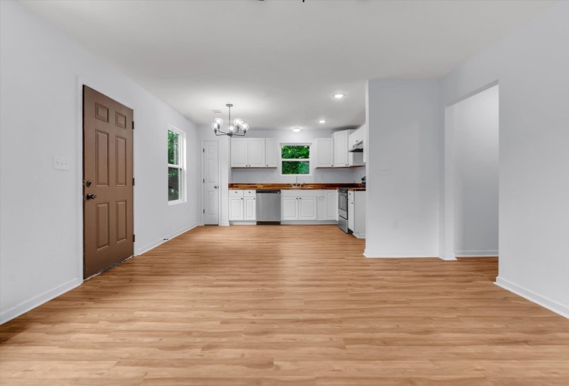 Open-concept living space with wood-finish flooring, white walls, and a modern chandelier