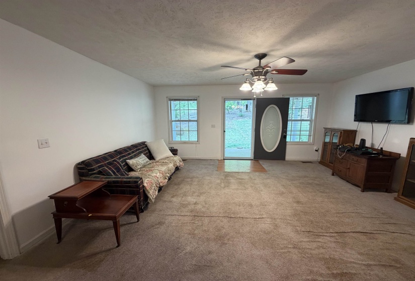 Living area with light colored carpet, a textured ceiling, and a ceiling fan