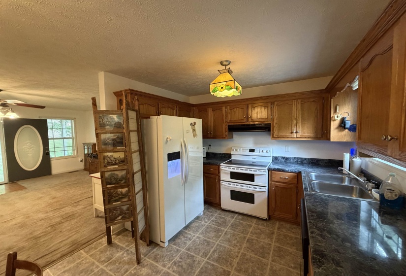 Kitchen with dark countertops, white appliances, wood finish cabinetry, a ceiling fan, and a textured ceiling