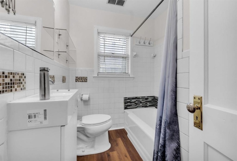 Bathroom featuring a white tile surround, mosaic accent tiles, a white vanity with a rectangular basin, wood-finish flooring, and a shower/tub combination
