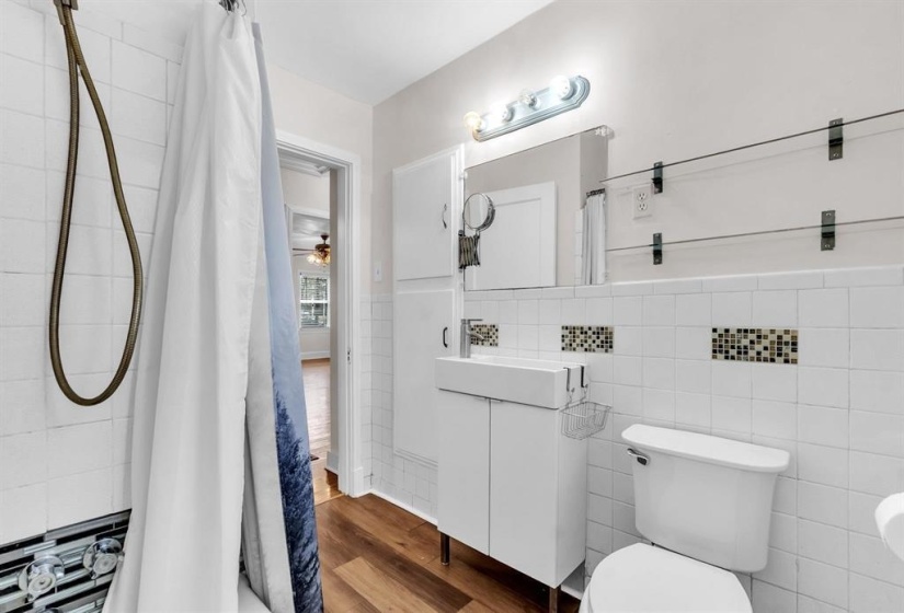Bathroom featuring white subway tile surround with mosaic accents, a modern vanity with integrated sink, and wood-finish flooring