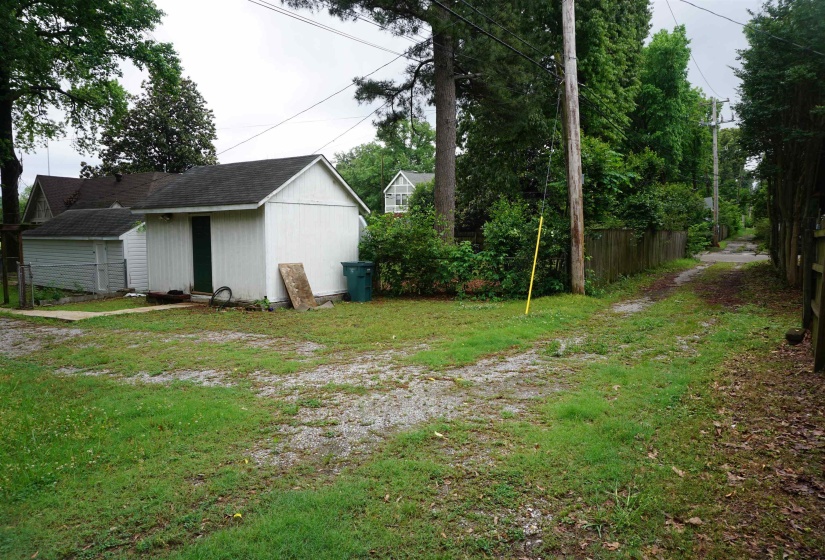 Detached outbuilding with white siding and a dark roof, featuring a single green door
