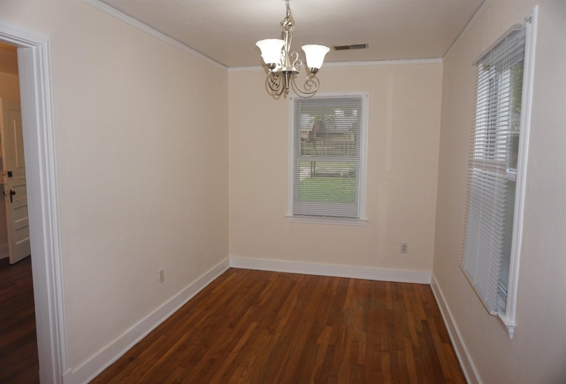 Interior space featuring wood-finish flooring, light-toned walls, crown molding, and two windows with blinds