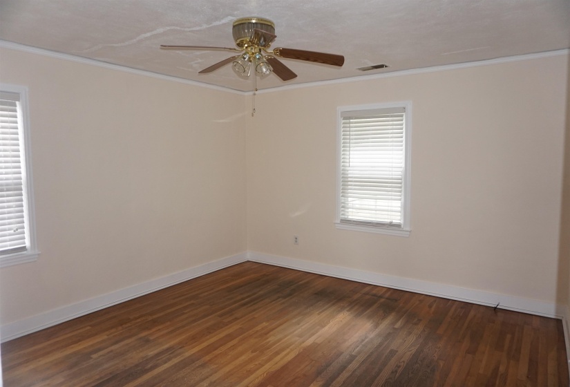 Spacious interior room featuring wood-finish flooring, two windows with blinds, and a ceiling fan with integrated lighting