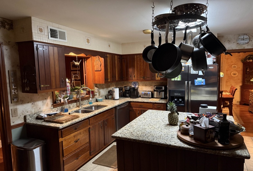 U-shaped kitchen featuring wood cabinetry, light-toned granite countertops, a double basin stainless steel sink, and a center island with granite counter
