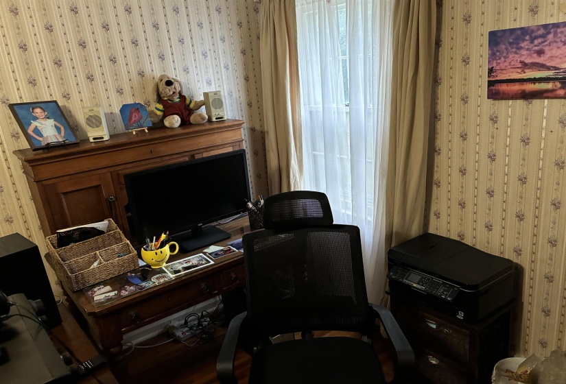 Room featuring patterned wallpaper, a single window with sheer and opaque drapes, and wood-finish flooring