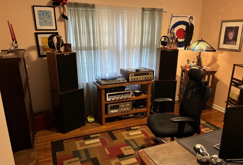Room featuring wood-finish flooring, light-colored walls, and a large window with sheer white curtains