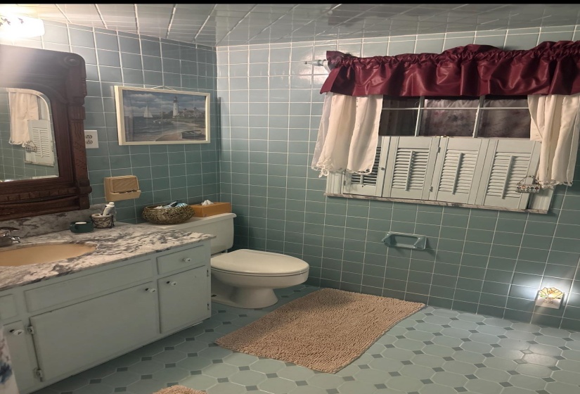 Bathroom featuring floor-to-ceiling blue tile, a white vanity with a marble-finish countertop, and a built-in window with white louvered shutters