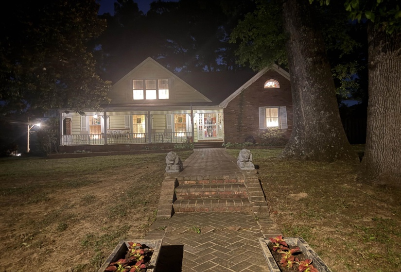Two-story residence featuring a combination of brick and siding exteriors, a covered front porch, a brick walkway, and mature trees