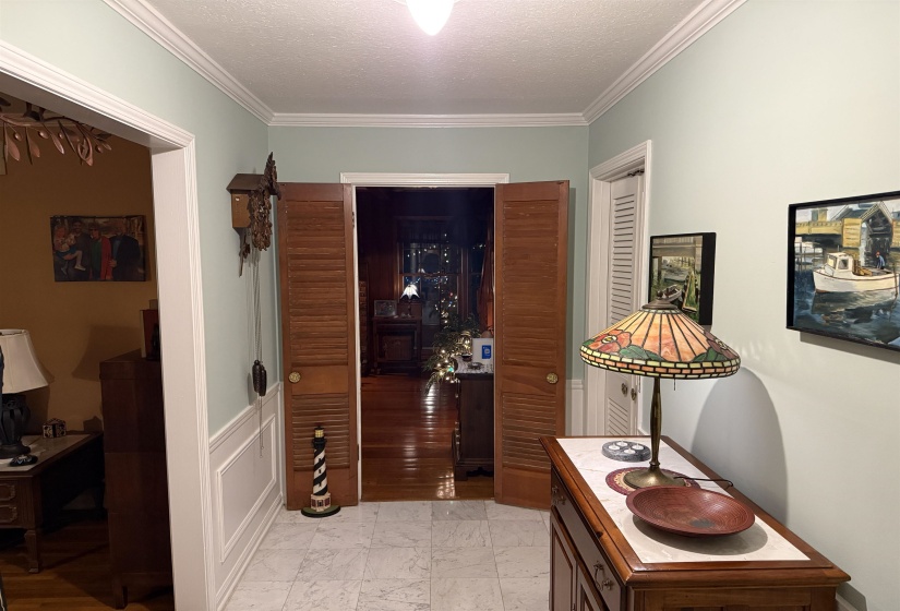 Entryway featuring marble-look tile flooring, wainscoting, and crown molding