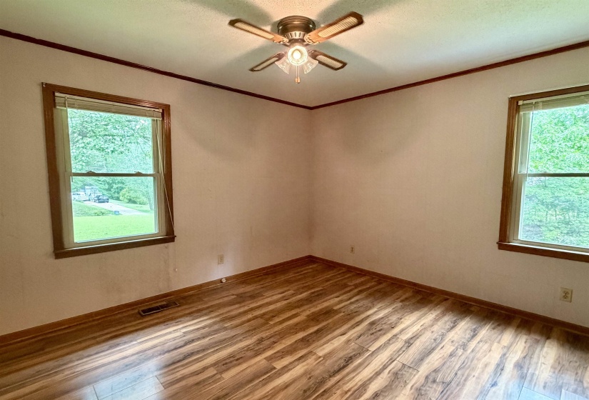 Room featuring wood-finish flooring, two large windows with wood trim, and a ceiling fan with integrated lighting