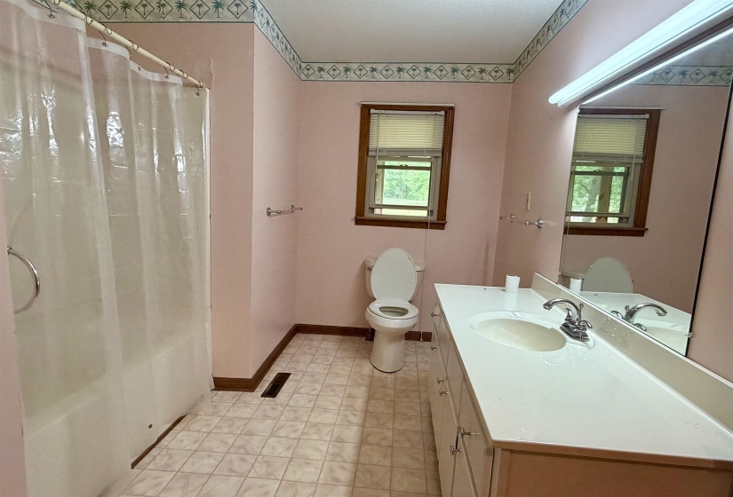 Bathroom featuring a single vanity with an integrated sink, a built-in tub with a shower, a toilet, a window with horizontal blinds, and patterned floor tiling