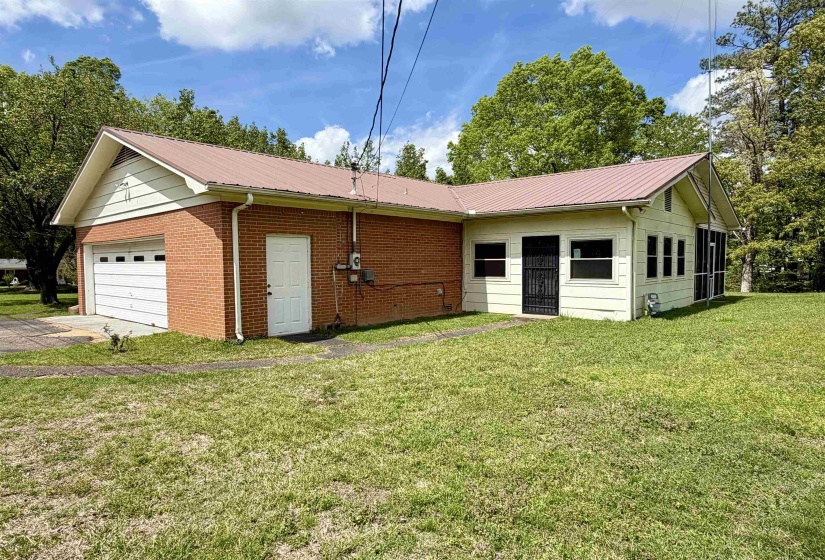 Exterior featuring a brick and siding facade with a metal roof, attached garage, screened porch, and mature trees