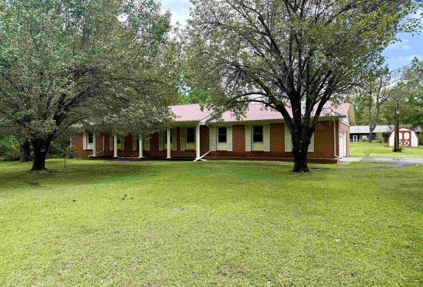 Brick exterior residence featuring a red metal roof, white porch columns, white window shutters, and an attached garage