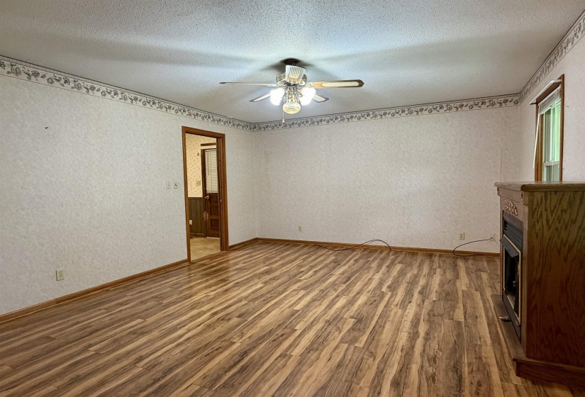 Spacious room featuring wood-finish flooring, a ceiling fan with integrated lighting, a built-in wooden mantel, and a window with wood trim