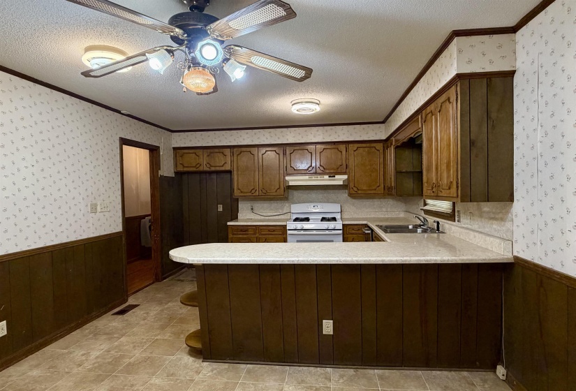 Kitchen featuring a peninsula with a light-colored countertop, wood-finish cabinetry, built-in range, and a ceiling fan with integrated lighting