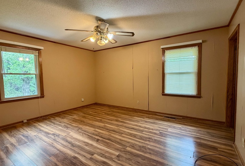 Spacious room featuring wood-finish flooring, two windows with wooden trim, a ceiling fan with integrated lighting, and neutral-toned wall paneling