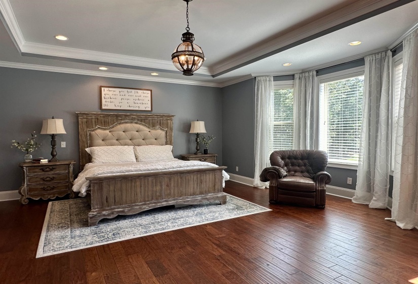 Bedroom with a raised ceiling, dark wood-style flooring, recessed lighting, crown molding, and a chandelier