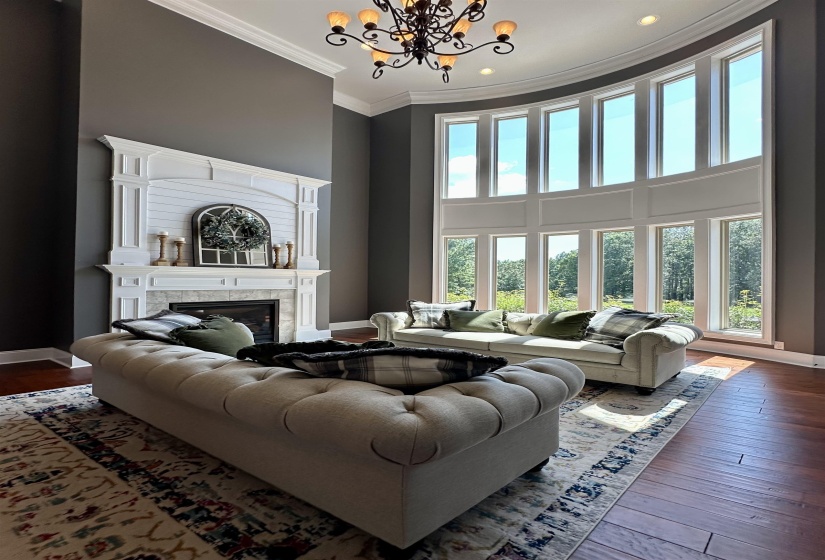 Living room with ornamental molding, a towering ceiling, wood-type flooring, a glass covered fireplace, and a chandelier
